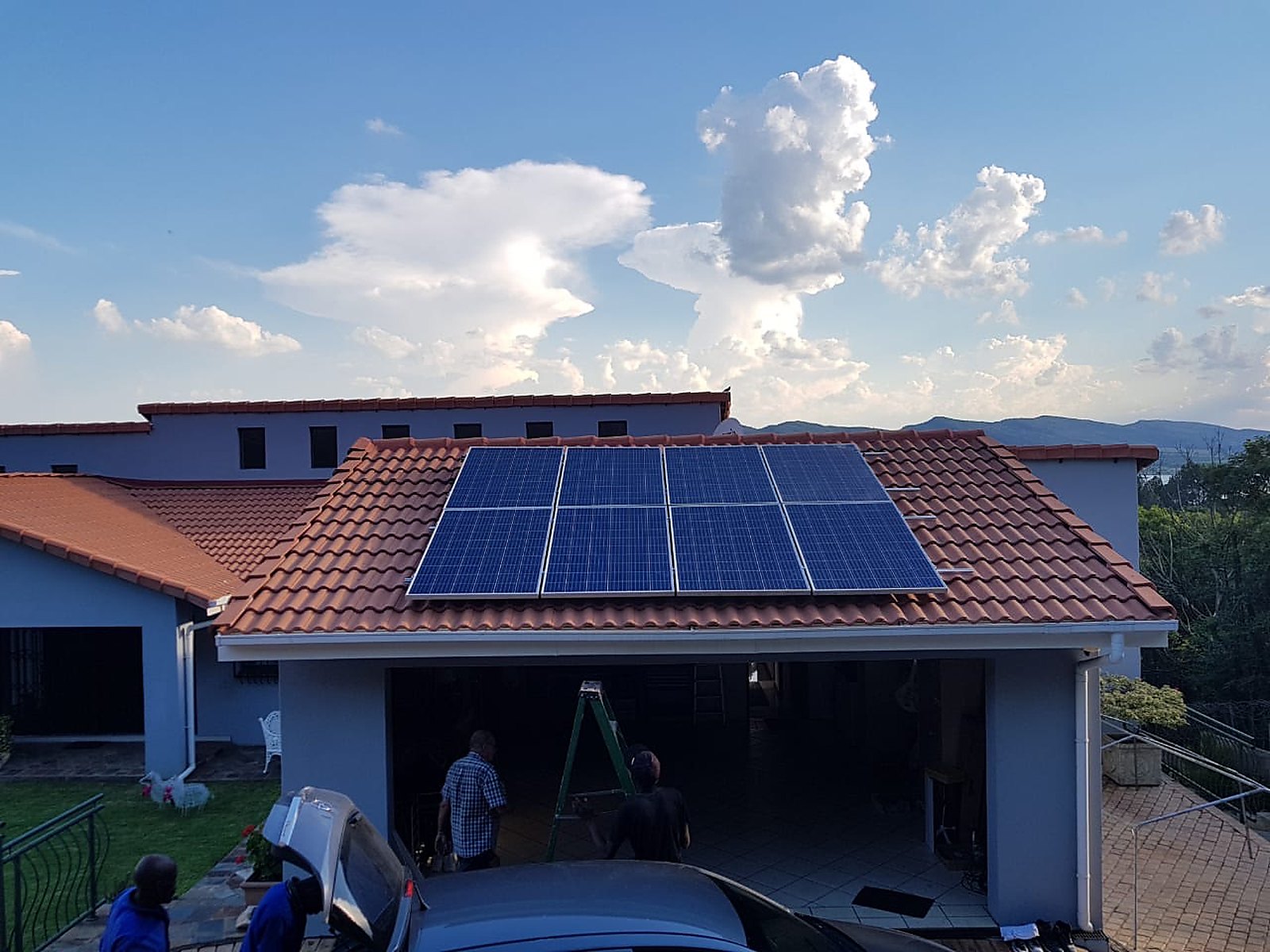 Eight solar panels fitted to the tiled garage roof of a house, with the installation crew working below.
